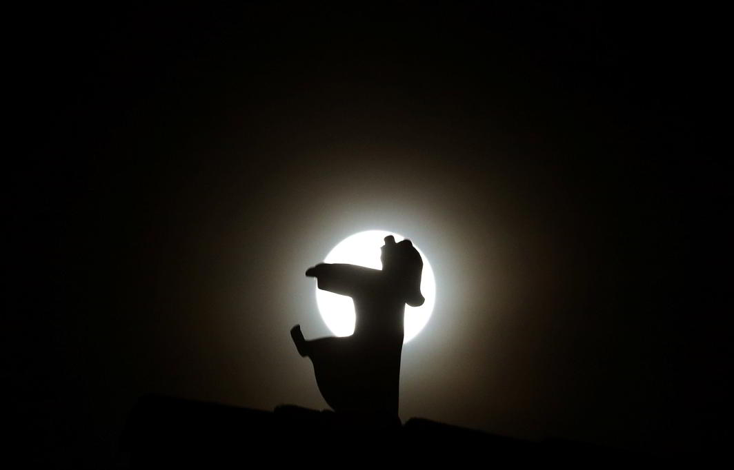 NO CHOICE BUT TO FOLLOW THAT CALL: A ceramic sleepwalker toy is silhouetted against the full moon on a roof in Hanau, 30km outside Frankfurt, Germany, Reuters/UNI